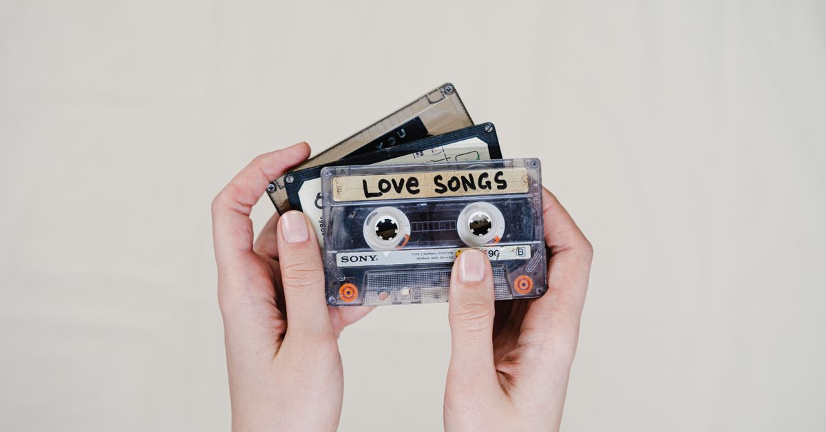 Hands holding cassette tapes labeled 'Love Songs', highlighting 90s nostalgia.